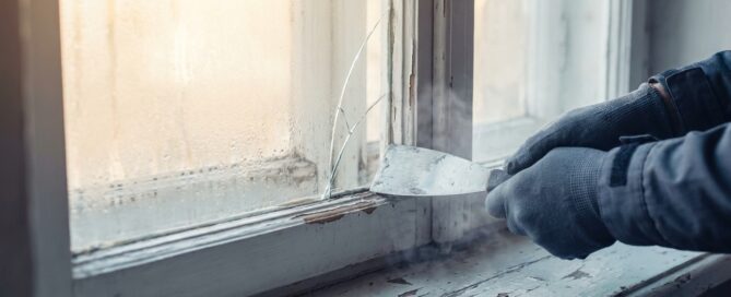Handwerkerhände entfernen eine beschlagene alte Isolierglasscheibe aus einem Altbaufenster