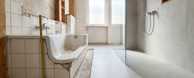 Altes Bad mit hoher Wannenkante neben neu gebauter schwellenloser Walk-In-Dusche mit Glaswand